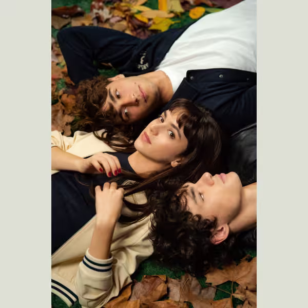 地面に落ち葉が散った場所に、男女三人が寄り添って横たわっている構図のポスター。中央の人物がカメラの方を見つめている。