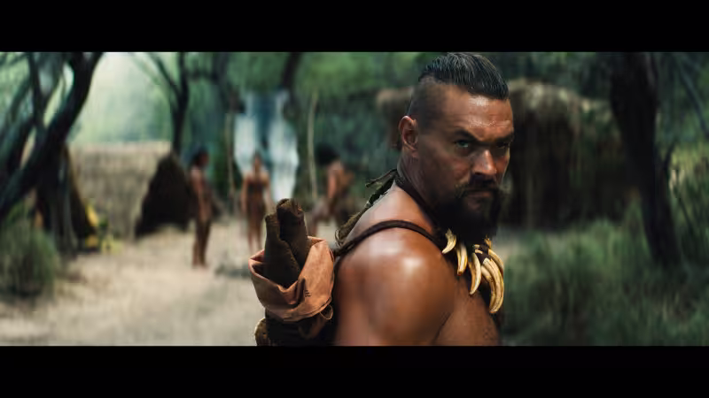Apple TV+『チーフ・オブ・ウォー』でジェイソン・モモアが戦士として部族の村を背景に鋭い眼差しで振り返るシーン