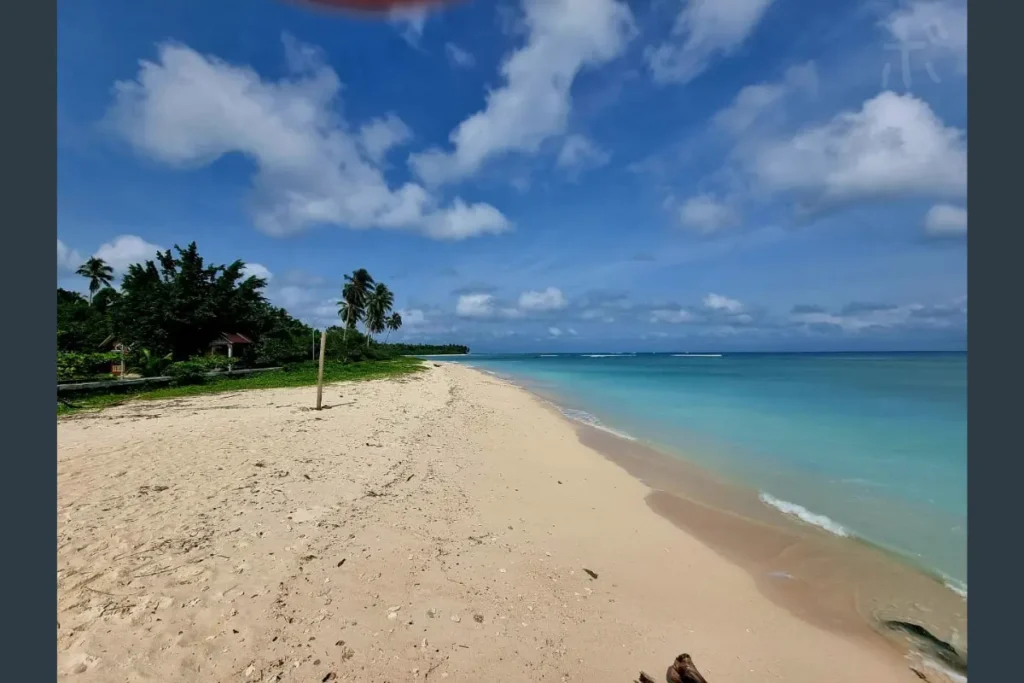 A view of a quiet white sand beach with blue skies and clear waters.