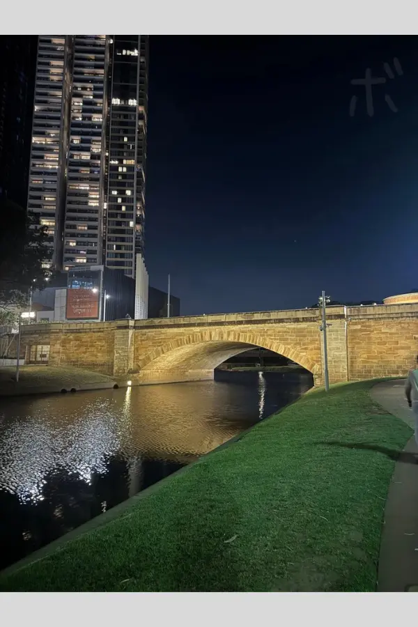 A view of the stone bridge over the river in Parramatta and the skyscrapers behind it, taken at night.