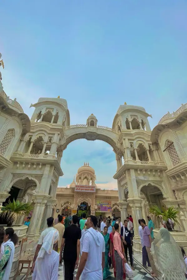 インドのISKCON寺院の入口に集まる参拝者たちと、美しい白い建築の風景