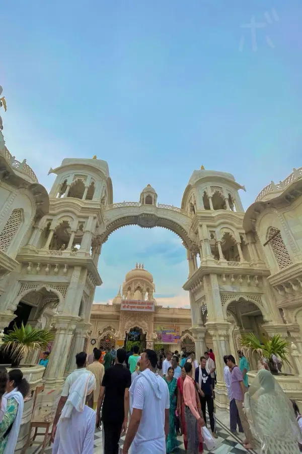 Worshippers gather at the entrance of an ISKCON temple in India with a view of the beautiful white architecture.