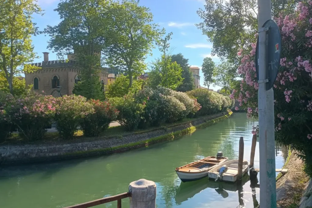 ヴェネツィア・リドの花に囲まれた運河と、小舟が静かに浮かぶ水辺の風景。