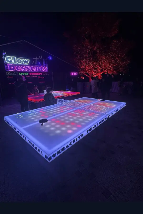 A view of the event site at night when people play on the glowing ping-pong table