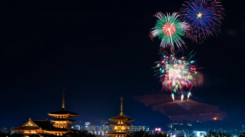 夜空に色鮮やかな花火が上がり、ライトアップされた寺院の塔が並ぶ日本の夏の夜景。