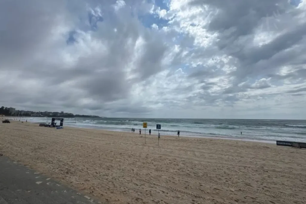 A quiet view of Manly Beach beneath a vast sky, where drifting clouds and gentle waves shape the rhythm of everyday life.