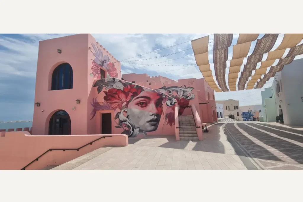 女性の顔の壁画が描かれたピンク色の建物