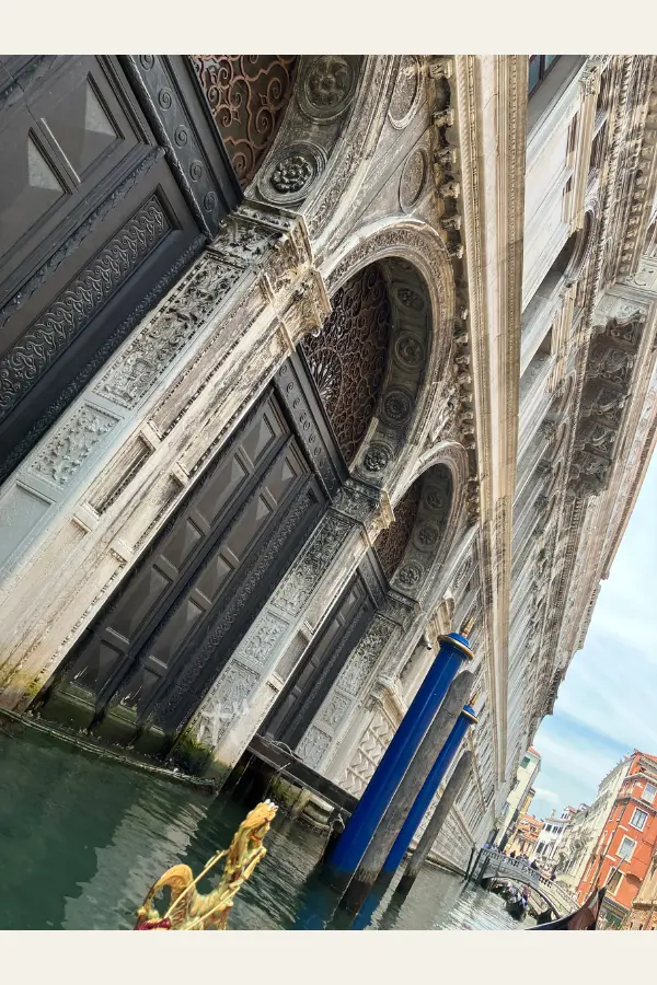 ゴンドラから見上げた、ヴェネツィアの歴史的な建物の装飾。青い係留杭と運河が写っている。