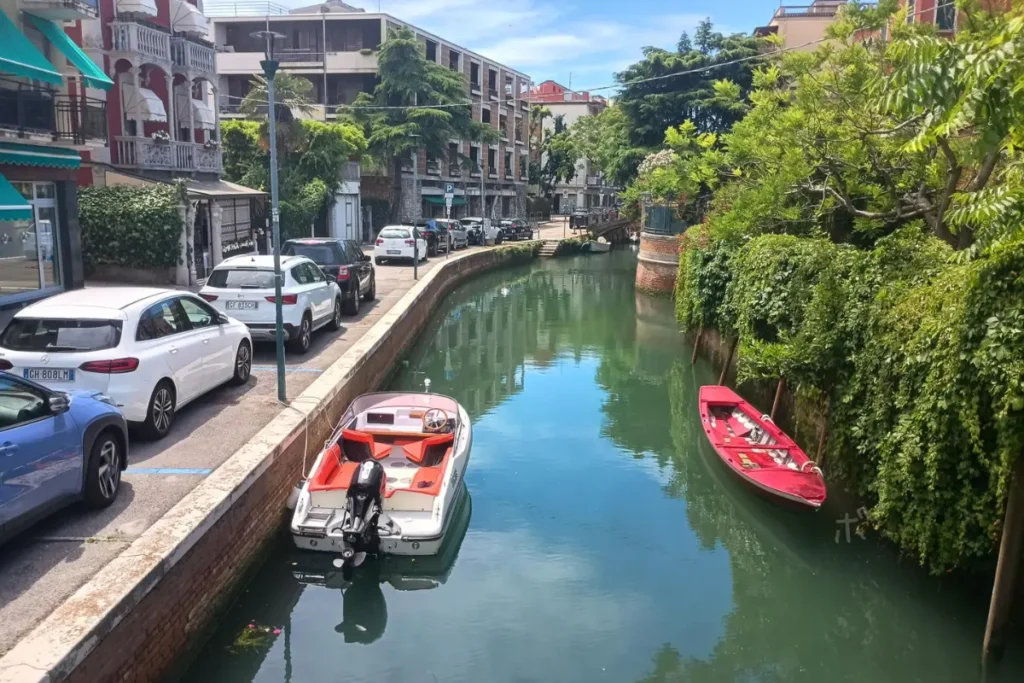 ヴェネツィア・リドの住宅街を流れる運河に、赤い小舟と白いボートが浮かぶ風景。