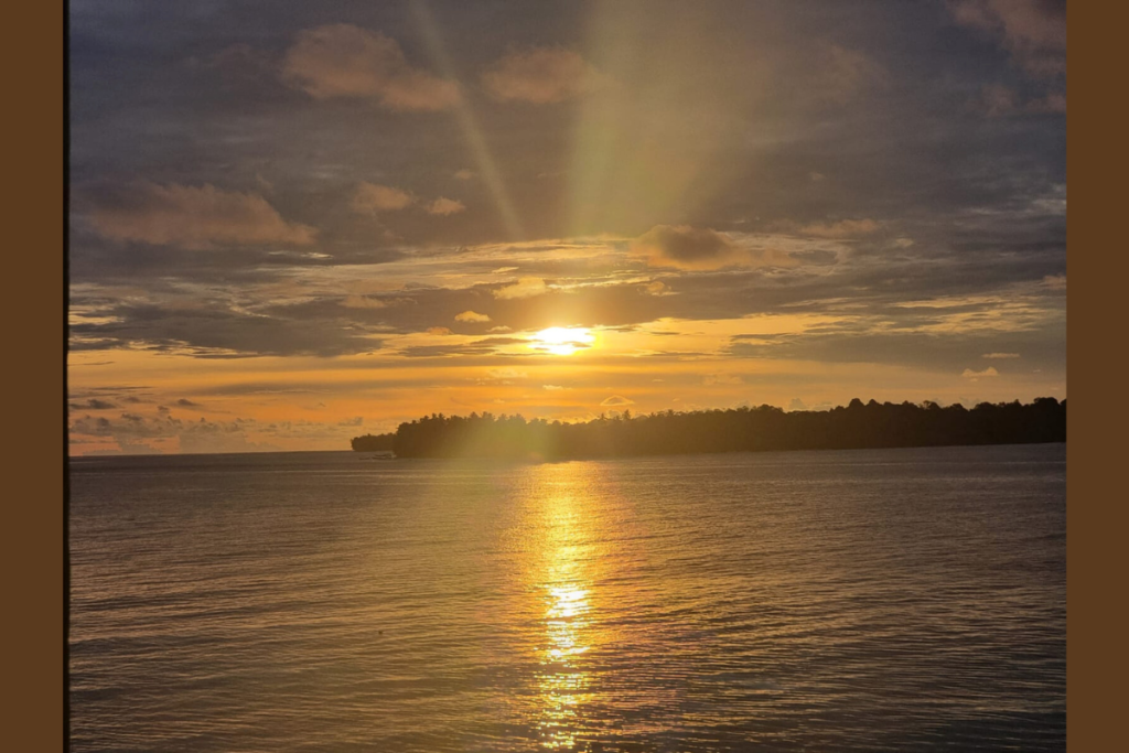 島の向こうに沈みかけた夕日が、海面にまっすぐな光を落としている風景。