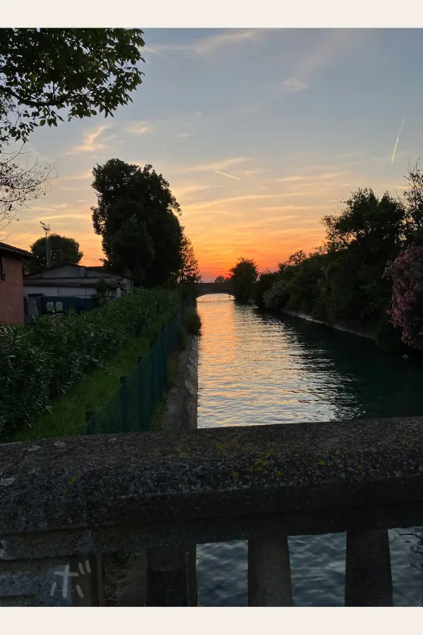 ヴェネツィア・リドの細い運河の先に夕陽が沈み、水面がオレンジ色に染まっている風景。