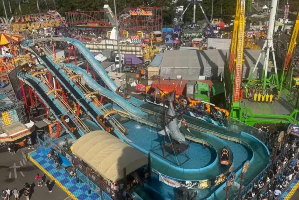 シドニー・イースター・ショーの遊園地エリアを上から見下ろした風景。ウォーターライドやアトラクション、人々の賑わいが広がるSeen Through Someone’s Eyesシリーズのアイキャッチ画像。
