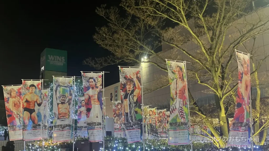 東京ドーム周辺に並ぶ、棚橋弘至や新日本プロレスの選手たちののぼり旗。夜のライトに照らされ、イッテンヨン当日の熱気が伝わる風景。