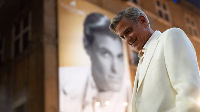 ジェイ・ケリーの公式ビジュアル。ジョージ・クルーニーがジェイ・ケリーのポスターの前に立つ姿。