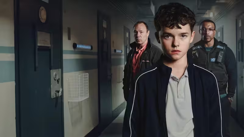 少年と刑事たちが無機質な拘置施設の廊下に立つ、社会派ドラマ『アドレセンス』の緊張感あるメインビジュアル